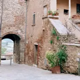 Antico vicolo con arco in pietra, tipico dei borghi vicino Rapolano Terme. Scale in pietra e piante in vaso aggiungono fascino.