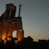 Il teatro romano di Volterra illuminato di sera, con le sue antiche colonne che emergono dall'ombra.