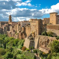 Un borgo arroccato su una rupe, con case in pietra e un campanile svettante, sembra una piccola Gerusalemme sotto un cielo azzurro e nuvoloso.