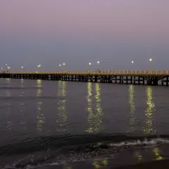 Il pontile di Forte dei Marmi illuminato al crepuscolo, con le luci che si specchiano sul mare calmo.
