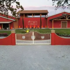 L'ingresso della Tenuta di Vaira a Bolgheri, con cancelli in rame e bianco, edifici rossi e un prato curato.