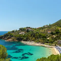 Incantevole baia con acque cristalline, spiagge dorate e case arroccate sulle colline verdi, un sogno di città toscane sul mare.