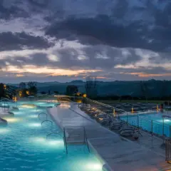 Piscine termali illuminate a Rapolano Terme al tramonto, con un cielo drammatico e colline toscane sullo sfondo.