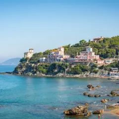 Panorami mozzafiato di Castiglioncello, Italia, con ville storiche affacciate sul mare turchese e una spiaggia animata.