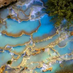 Cascate naturali di acqua turchese in un thermal spa Tuscany, con una persona che si rilassa tra le rocce calcaree.