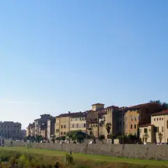 Edifici storici e una torre medievale si affacciano sul fiume nel pescia centro storico, sotto un cielo azzurro.