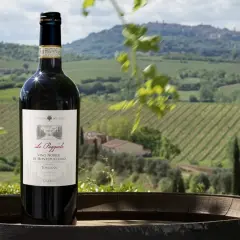 Bottiglia di Vino Nobile di Montepulciano su una botte, con vigneti e colline toscane sullo sfondo. Un invito a una visita cantina Montepulciano.