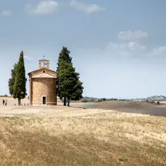 Iconica chiesetta Val d'Orcia, con cipressi e colline ondulate sotto un cielo nuvoloso.