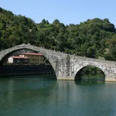 Il Ponte del Diavolo, con i suoi archi in pietra, attraversa un fiume verdeggiante, circondato da colline boscose.