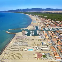 Vista aerea di Marina di Grosseto con spiaggia affollata, porto turistico pieno di barche e case con tetti rossi.