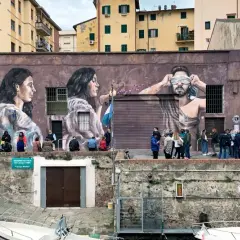Un imponente murales livornese raffigura tre volti, uno bendato, con persone che osservano l'opera d'arte.