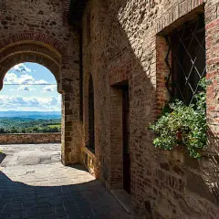 Un vicolo in pietra a San Gusmè, con un arco che rivela un paesaggio collinare toscano.