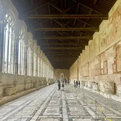 Corridoio del Camposanto Monumentale di Pisa con arcate gotiche, affreschi antichi e sarcofagi romani.