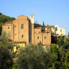 Il convento San Francesco a San Miniato, con la sua imponente struttura in mattoni rossi, si staglia tra il verde degli alberi e il cielo azzurro.