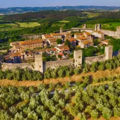 Il centro storico di Monteriggioni, un borgo medievale fortificato, si erge su una collina circondato da mura e torri, immerso nel verde della campagna toscana.