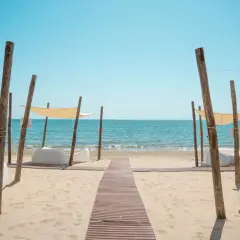 Un percorso in legno conduce al **follonica mare**, dove lettini bianchi e tende color crema invitano al relax sotto il sole.
