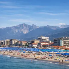 Una vivace spiaggia libera al Lido di Camaiore, con montagne imponenti sullo sfondo e un mare azzurro.