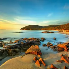 La Cala Martina al tramonto, con rocce scure e sabbia dorata bagnata da un mare calmo e cielo sfumato.