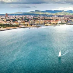 Un veliero solca il mare di Livorno, con la città e le colline sullo sfondo.