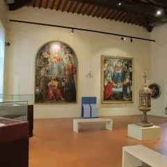Interno di una sala dei musei di Arezzo con dipinti rinascimentali, un'urna e teche espositive.