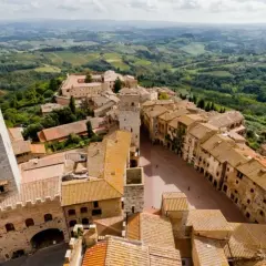 Panoramica aerea di San Gimignano, con le sue torri medievali che svettano tra i tetti di tegole rosse. Un paesaggio incantevole, tipico dei borghi vicino San Gimignano, immerso nel verde delle colline toscane.