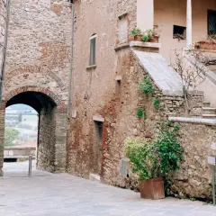 Antico vicolo con arco in pietra, tipico dei borghi vicino Rapolano Terme. Scale in pietra e piante in vaso aggiungono fascino.