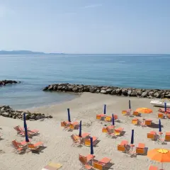 Spiaggia attrezzata con lettini e ombrelloni arancioni, mare azzurro e scogli. Un sogno di vacanza a Pratoranieri Follonica.