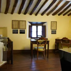 Interno di una casa museo, con travi a vista, una scrivania con macchina da cucire, un busto e un abito in esposizione. Un luogo dove le case della memoria prendono vita.