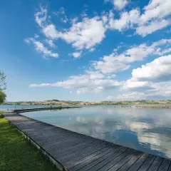 Passerella in legno su un lago tranquillo, con colline ondulate sullo sfondo. Un luogo idilliaco in Valdichiana, dove la natura incontra la serenità.