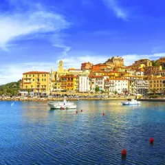 Vista del porto di Porto Santo Stefano, con case colorate che si arrampicano sulla collina e barche sull'acqua blu.
