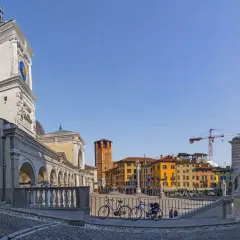 La piazza della Libertà, con la sua torre dell'orologio, edifici colorati e due biciclette in primo piano, sotto un cielo azzurro.