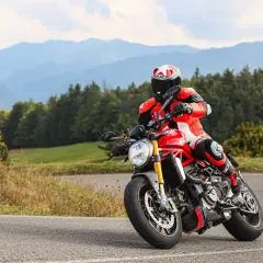 Motociclista in tuta rossa affronta una curva sul passo del giogo, con montagne sullo sfondo.