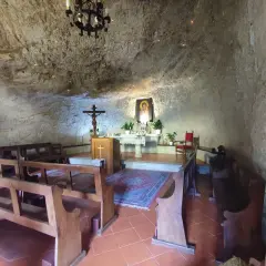 Interno dell'eremo di Calomini, con panche in legno, altare, crocifisso e un'icona sacra incastonati nella roccia.