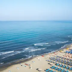 Ampia spiaggia attrezzata al **Lido di Camaiore**, con file ordinate di ombrelloni blu e arancioni che si estendono verso il mare calmo e azzurro.