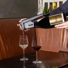 Versando vino bianco da una bottiglia con un erogatore Coravin, accanto a un bicchiere di vino rosso. Un tipo di vino da scoprire.