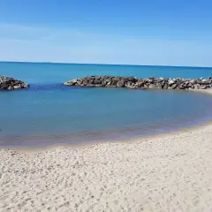 Spiaggia di Marina di Pisa con acque calme e dighe frangiflutti in pietra.