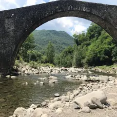 Il ponte di Castruccio, con il suo arco maestoso, sovrasta un fiume serpeggiante tra rocce e vegetazione lussureggiante.