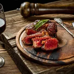 Bistecca succulenta con rosmarino, accompagnata da un bicchiere di vino tannico e posate d'argento su un tagliere di legno rustico.