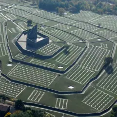 Vasta distesa di tombe bianche disposte in file ordinate, con un imponente monumento centrale. Il cimitero tedesco del Passo della Futa, un luogo di memoria.