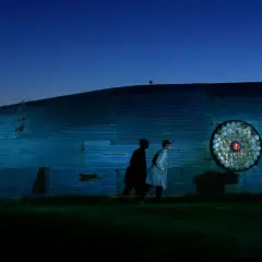 Due uomini osservano un'installazione artistica a forma di balena nel giardino, un viaggio di ritorno verso la luce.