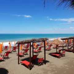 Marina di Bibbona spiagge più belle: lettini rossi e ombrelloni di paglia sotto un cielo azzurro, con il mare calmo all'orizzonte.