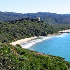 Spiaggia delle bandite di Scarlino, con mare azzurro, vegetazione lussureggiante e una villa in collina.