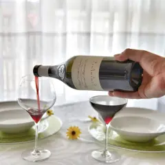 Versare vino rosso in un calice, un passo fondamentale per capire come si fa il vino rosso. La tavola è apparecchiata.