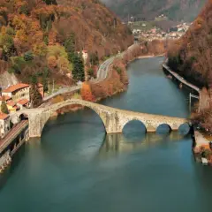 Il Ponte della Maddalena, con i suoi archi irregolari, attraversa un fiume circondato da colline autunnali e case colorate.