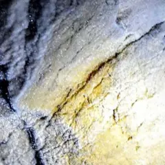 Esplorazione della grotta turistica Antro del Corchia: rocce scintillanti e un casco illuminato da una torcia.
