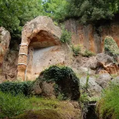 Antica tomba etrusca scavata nella roccia, con un pilastro decorato da fasce metalliche, immersa nel verde della necropoli di Sovana.