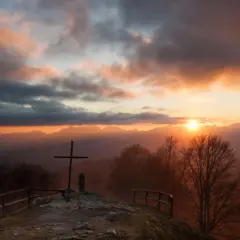 Croce in cima a una collina al tramonto, con montagne sullo sfondo. Un luogo suggestivo a San Pellegrino in Alpe.