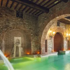 Piscina termale con archi in mattoni e pietra, cascate d'acqua e luci soffuse, un'oasi di relax nel paese di Venturina Terme.