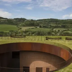 Un'avveniristica cantina toscana si fonde con il paesaggio collinare, con un tetto verde e un pozzo circolare in corten.