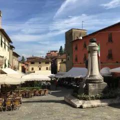Piazza soleggiata a Montecatini Alto con tavolini all'aperto e un monumento.